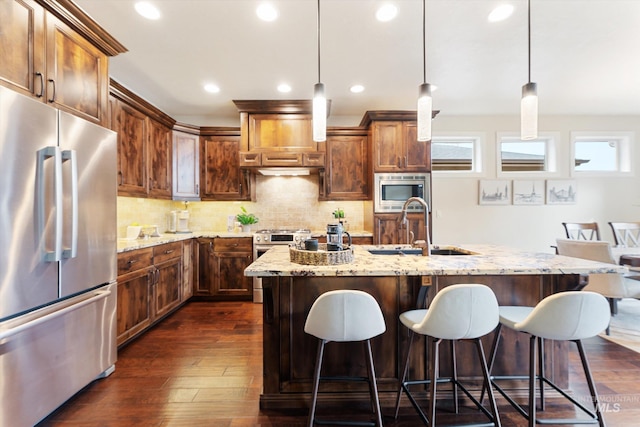 kitchen with a sink, light stone counters, dark wood-style flooring, and stainless steel appliances