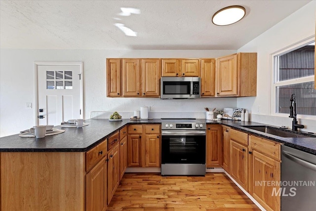 kitchen with sink, kitchen peninsula, stainless steel appliances, a textured ceiling, and light hardwood / wood-style flooring