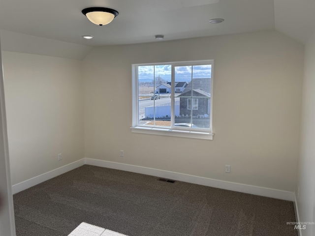 spare room featuring dark carpet, vaulted ceiling, visible vents, and baseboards