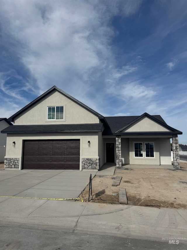 view of front of property featuring a garage, driveway, stone siding, and stucco siding