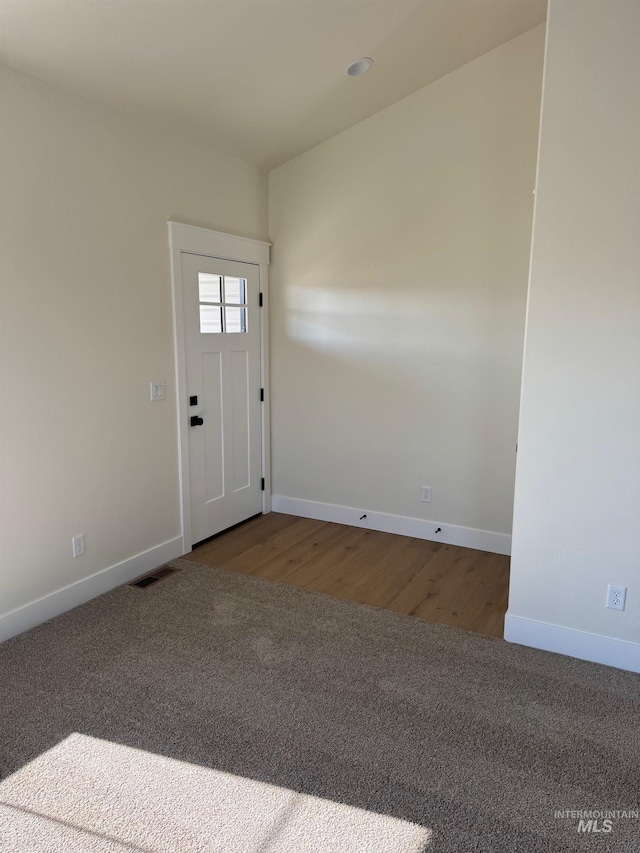 foyer entrance with visible vents, wood finished floors, baseboards, and carpet
