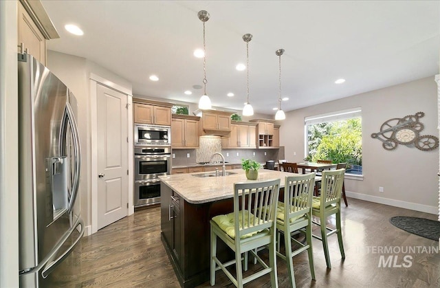 448 E Eaglewoods Ln, Eagle, ID 83616 - kitchen with appliances with stainless steel finishes, an island with sink, dark wood-style floors, a breakfast bar area, and decorative backsplash
