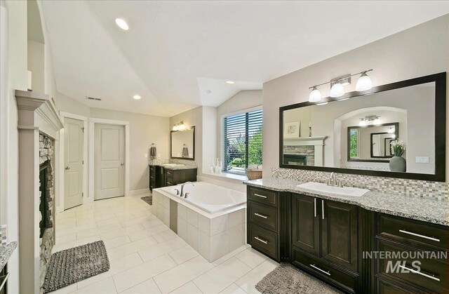 448 E Eaglewoods Ln, Eagle, ID 83616 - full bathroom featuring vaulted ceiling, tile patterned floors, a bath, a stone fireplace, and two vanities