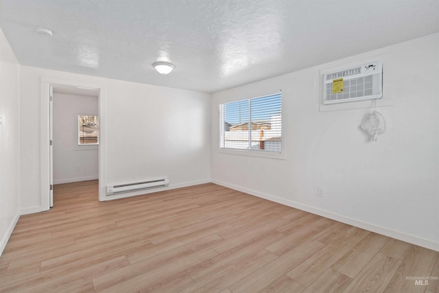spare room featuring an AC wall unit, baseboards, light wood-style floors, and baseboard heating