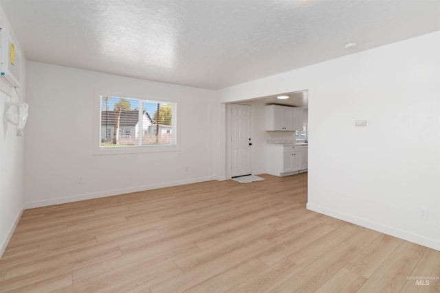 interior space featuring light wood-type flooring, baseboards, and a textured ceiling