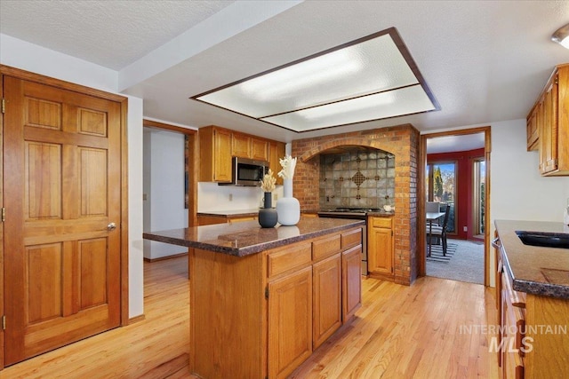 kitchen with a textured ceiling, stainless steel appliances, sink, light hardwood / wood-style flooring, and a kitchen island