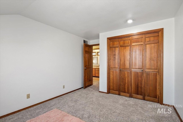 unfurnished bedroom featuring lofted ceiling, light carpet, and a closet