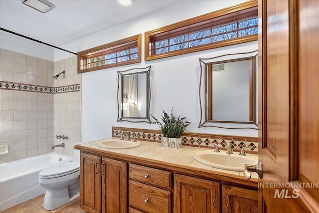 full bathroom with vanity, backsplash, tile patterned flooring, tiled shower / bath combo, and toilet