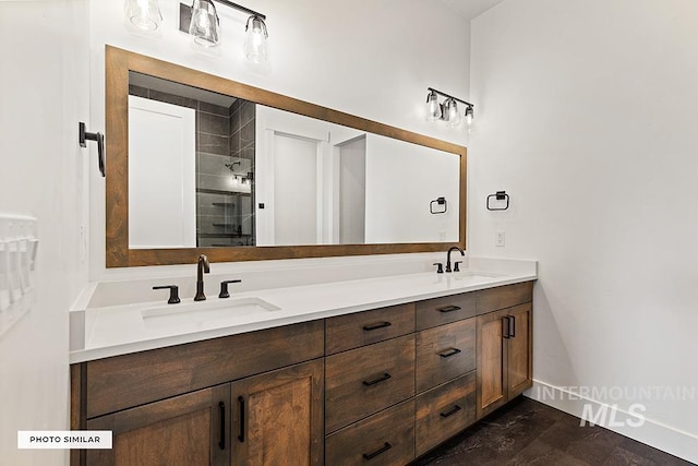 bathroom with a sink, baseboards, double vanity, and tiled shower