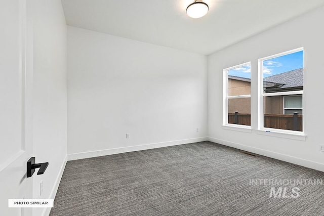 spare room featuring dark colored carpet and baseboards