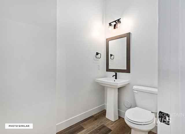 half bathroom with a sink, toilet, wood finished floors, and baseboards