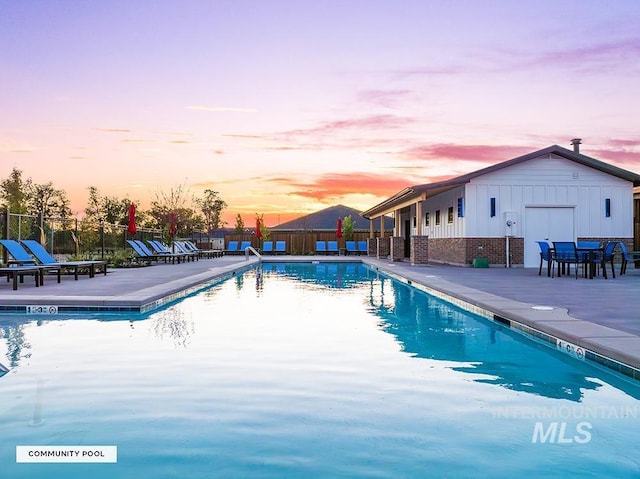 pool at dusk featuring a community pool, fence, and a patio area