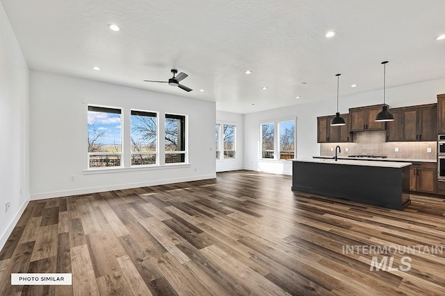 unfurnished living room featuring ceiling fan, recessed lighting, a sink, baseboards, and dark wood-style floors