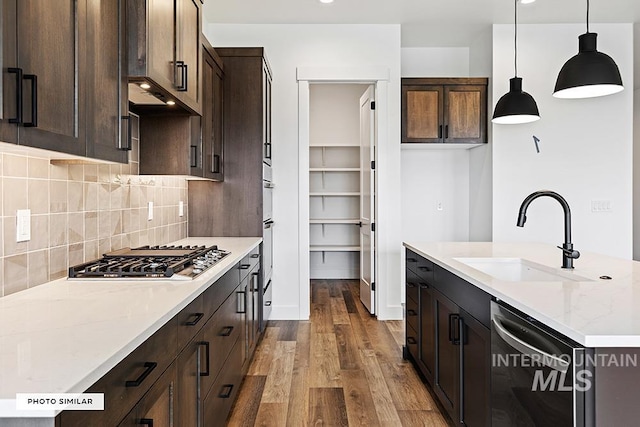 kitchen featuring backsplash, stainless steel appliances, pendant lighting, a sink, and wood finished floors
