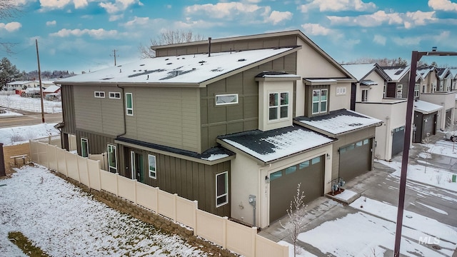 snow covered property with driveway, a residential view, an attached garage, fence, and board and batten siding