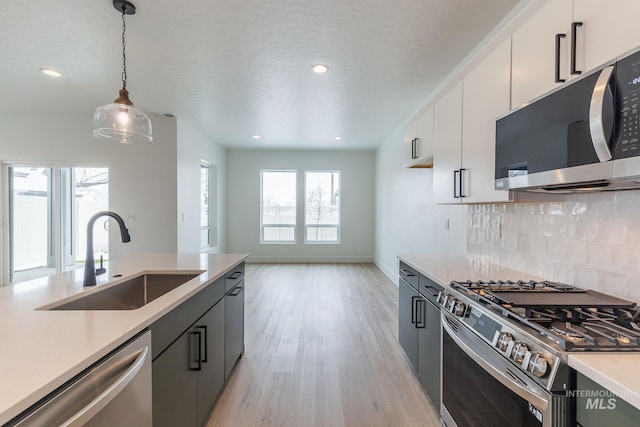 kitchen featuring a sink, light countertops, appliances with stainless steel finishes, backsplash, and decorative light fixtures