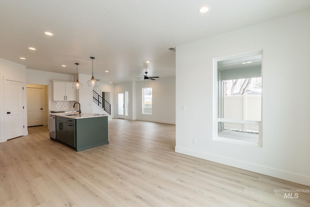 kitchen featuring open floor plan, a kitchen island with sink, light countertops, light wood-type flooring, and backsplash