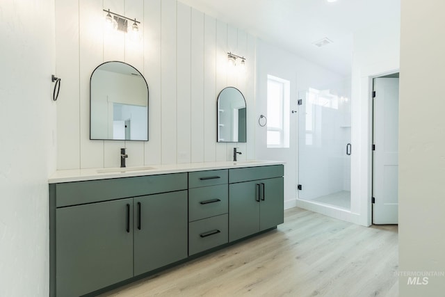 full bath with double vanity, wood finished floors, a sink, and a shower stall