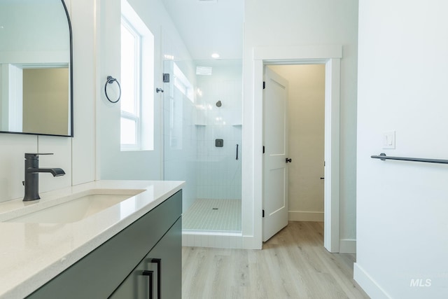 bathroom with a stall shower, wood finished floors, vanity, and baseboards