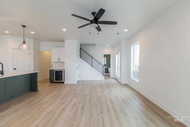 unfurnished living room with wine cooler, recessed lighting, baseboards, stairs, and light wood finished floors