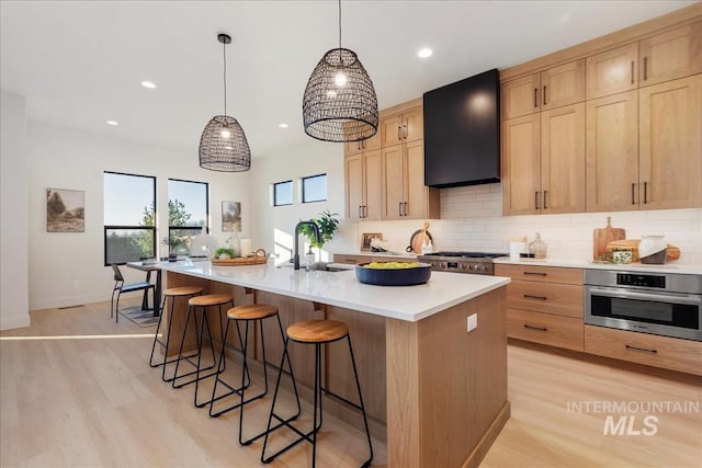 kitchen featuring appliances with stainless steel finishes, a center island with sink, light brown cabinets, and wall chimney exhaust hood