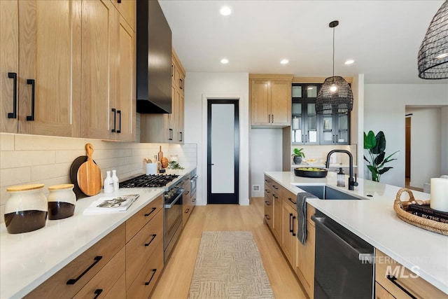 kitchen featuring sink, light hardwood / wood-style floors, wall chimney range hood, pendant lighting, and appliances with stainless steel finishes