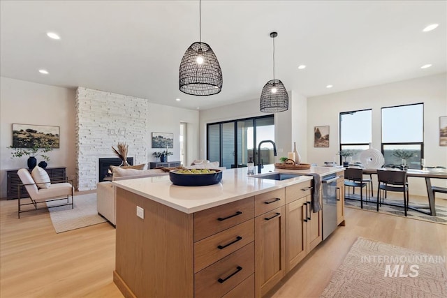 kitchen featuring sink, a center island with sink, a fireplace, and light hardwood / wood-style flooring