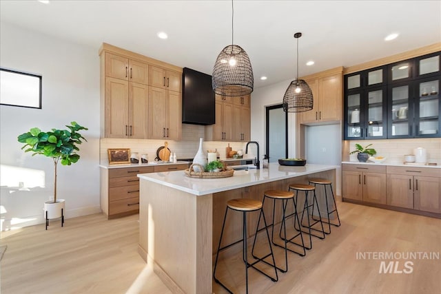 kitchen with light hardwood / wood-style floors, pendant lighting, decorative backsplash, and a center island with sink