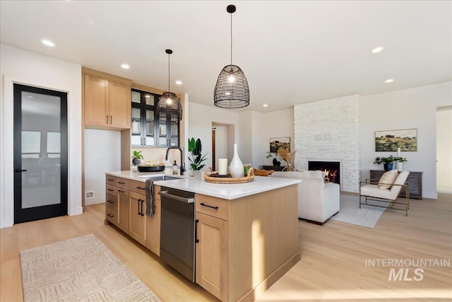 kitchen with sink, dishwasher, light brown cabinets, an island with sink, and a stone fireplace