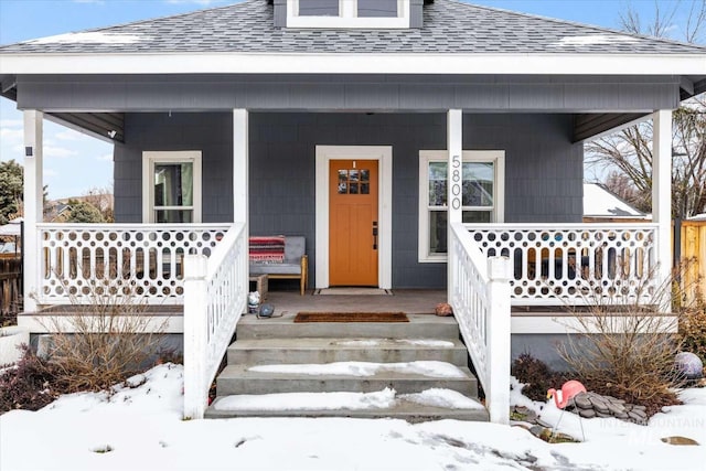 snow covered property entrance with covered porch and roof with shingles