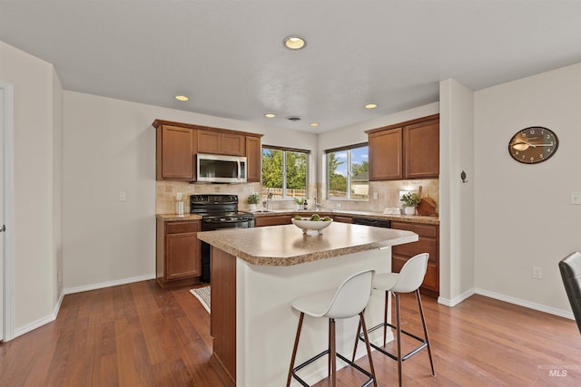 11422 W Darkwood St, Star, ID 83669 - kitchen featuring stainless steel microwave, black range with electric stovetop, dark wood finished floors, brown cabinetry, and decorative backsplash