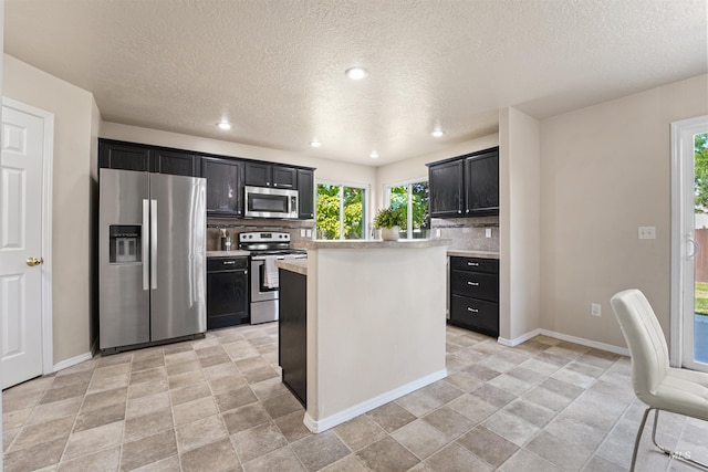 5217 Weston Ave, Caldwell, ID 83607 - kitchen featuring appliances with stainless steel finishes, dark cabinets, backsplash, light countertops, and a textured ceiling
