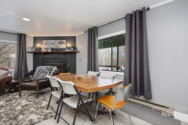 dining area with a fireplace, a baseboard radiator, light hardwood / wood-style floors, and a textured ceiling