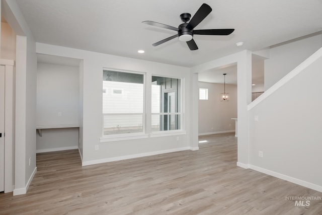 spare room with ceiling fan with notable chandelier and light wood-type flooring