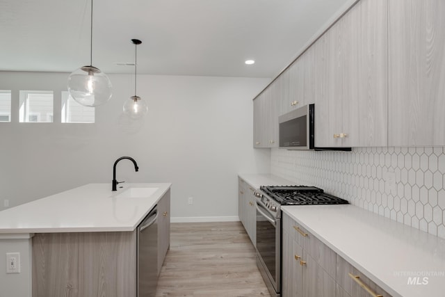 kitchen with light wood-type flooring, appliances with stainless steel finishes, backsplash, hanging light fixtures, and sink