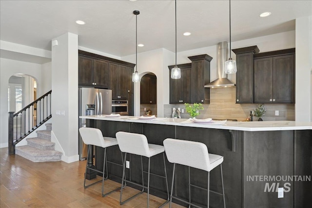 kitchen with decorative backsplash, arched walkways, appliances with stainless steel finishes, and wall chimney range hood