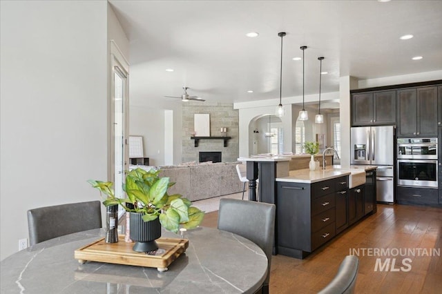dining room with ceiling fan, a stone fireplace, dark wood-type flooring, and recessed lighting
