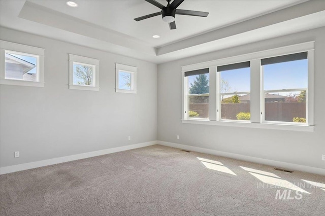 unfurnished room with ceiling fan, light carpet, a raised ceiling, baseboards, and visible vents