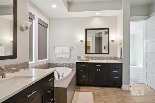 full bathroom featuring a bath, backsplash, two vanities, and a sink