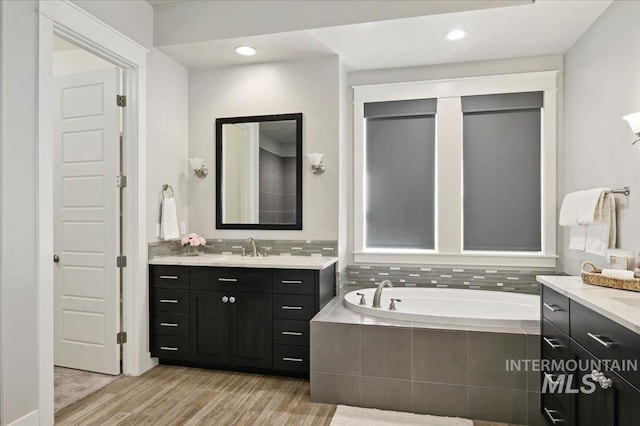 full bath with a bath, vanity, wood finished floors, and recessed lighting