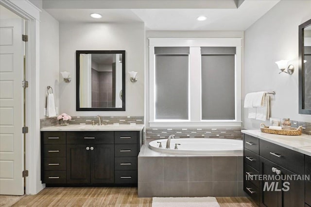 full bath with two vanities, wood finished floors, a garden tub, and a sink