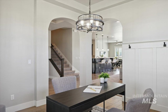 office with arched walkways, wood finished floors, baseboards, and an inviting chandelier