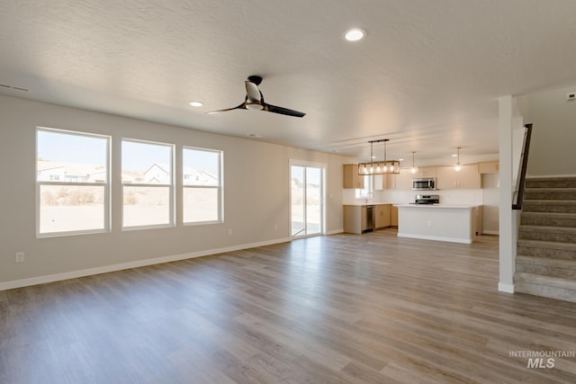 unfurnished living room featuring visible vents, stairway, light wood-style flooring, a textured ceiling, and a ceiling fan