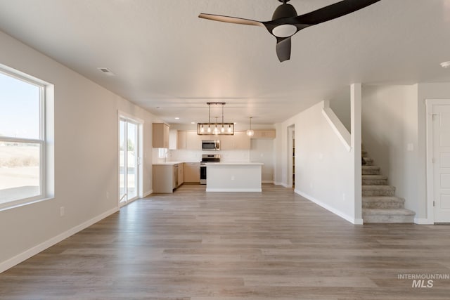 unfurnished living room with stairway, light wood-style flooring, a ceiling fan, and baseboards