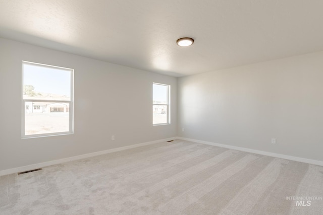 empty room with light colored carpet, visible vents, and baseboards