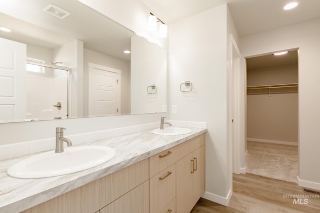 full bathroom with a sink, visible vents, a shower with shower door, and wood finished floors