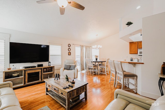 living area featuring vaulted ceiling, baseboards, ceiling fan with notable chandelier, and light wood-type flooring
