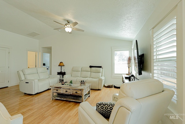 living room featuring visible vents, light wood-style floors, ceiling fan, a textured ceiling, and vaulted ceiling