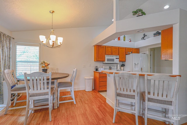 kitchen with an inviting chandelier, a breakfast bar, white appliances, brown cabinetry, and light wood-type flooring