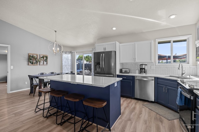 5174 N Rothmans Ave, Boise, ID 83713 - kitchen with stainless steel appliances, blue cabinetry, a kitchen breakfast bar, backsplash, and light wood-type flooring